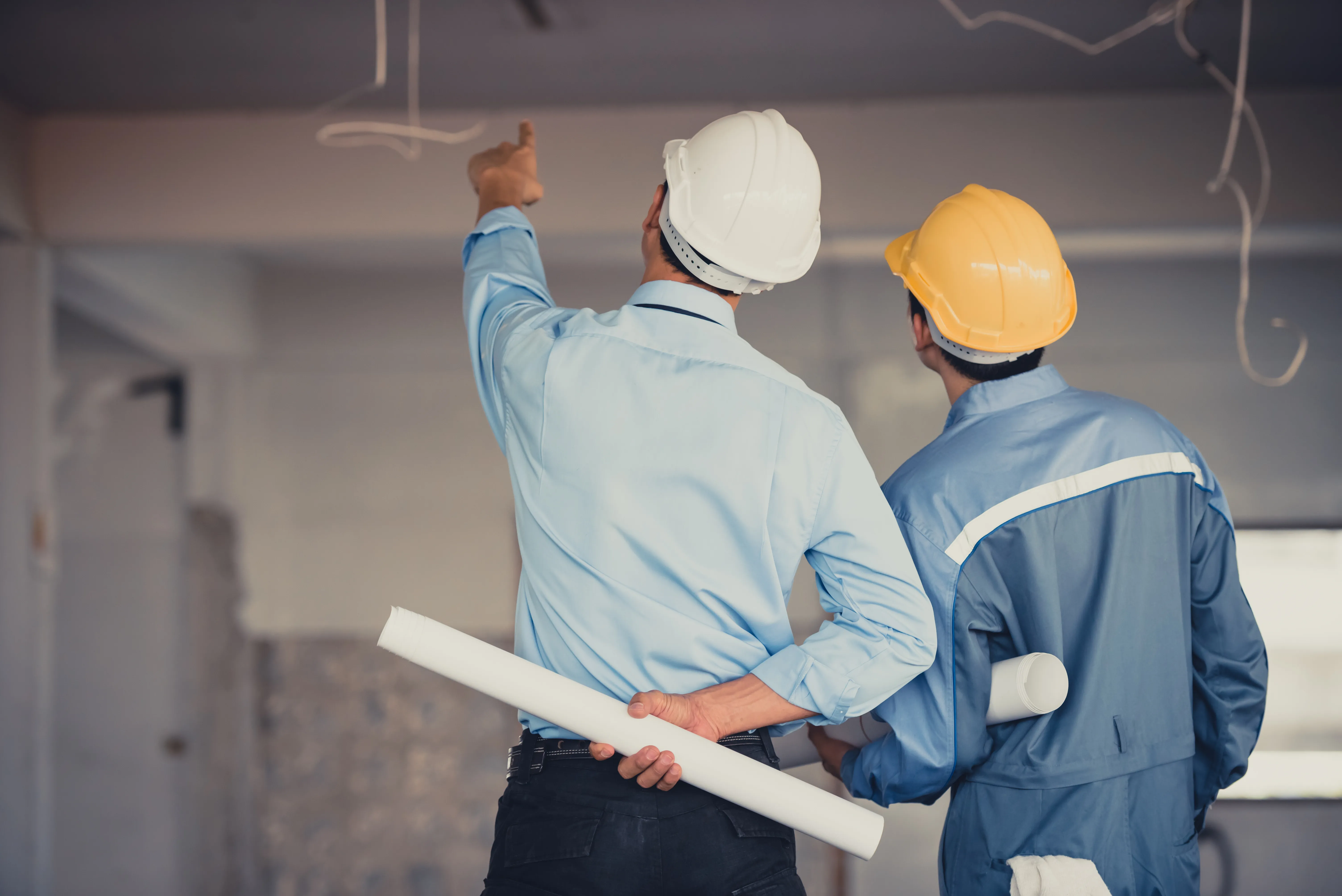 Two upright workers reviewing a ceiling at an indoor construction site