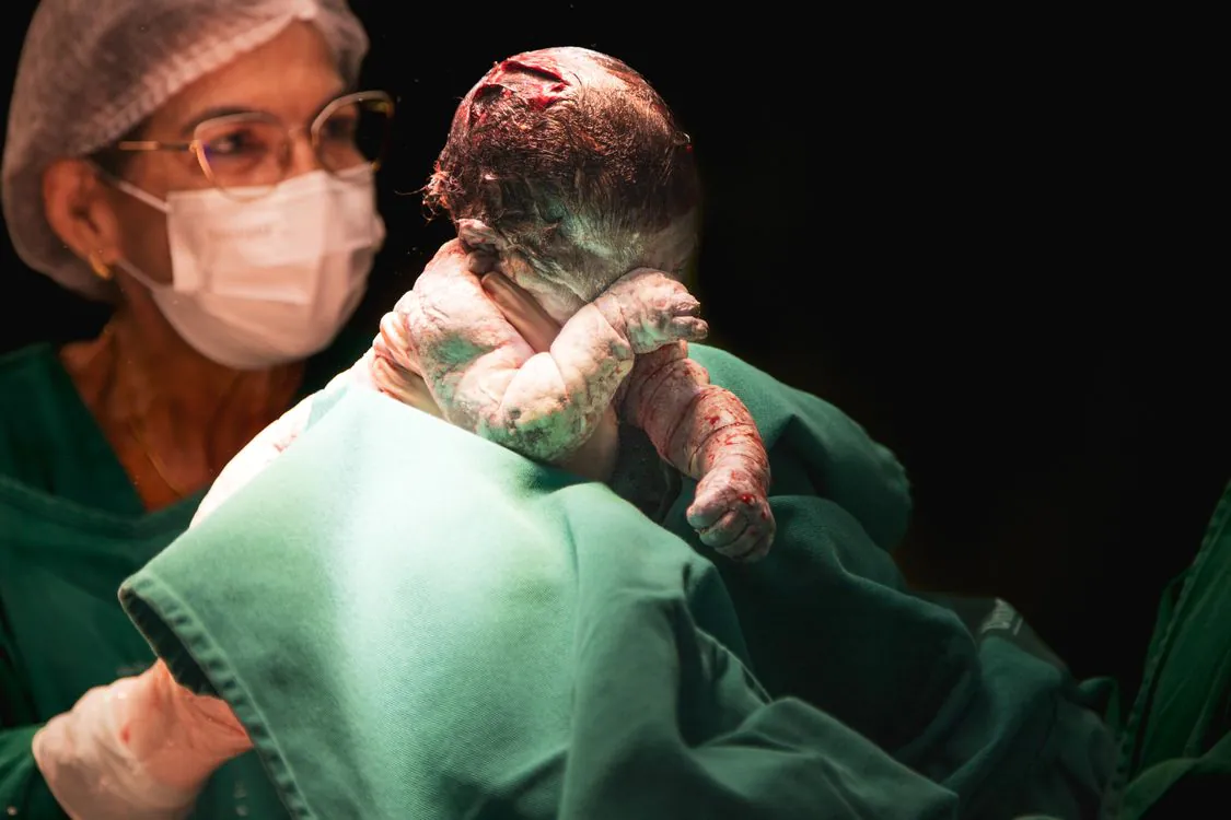 Newborn baby held by a midwife in a hospital delivery room