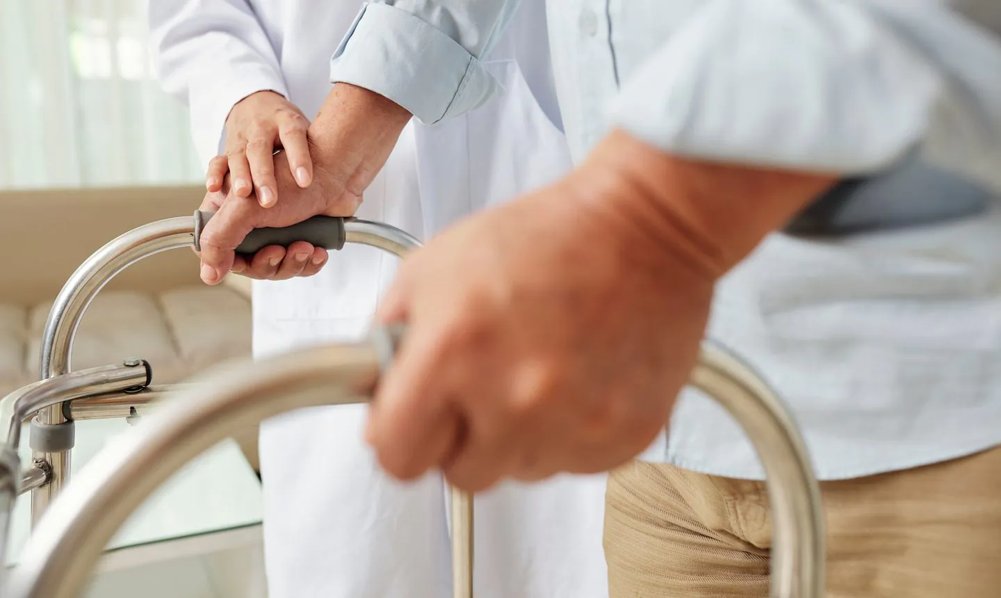 Patient relearning to walk with a walker as a clinician supports their hands after a serious injury