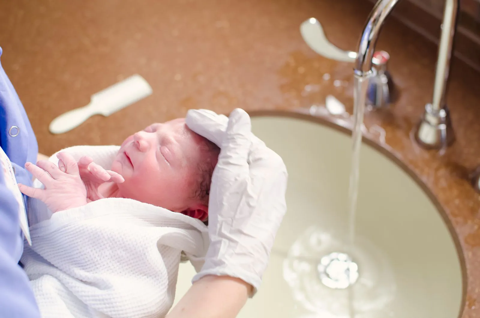 Nurse bathing a newborn baby in a hospital sink